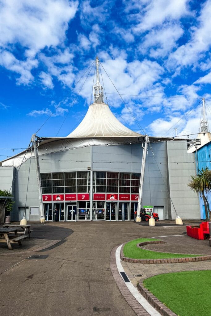 Butlins Tent Minehead The main entrance to the Butlins Minehead pavilion, featuring a large tent structure with white peaks against a blue sky. The entrance is modern with large glass doors and Butlins branding.